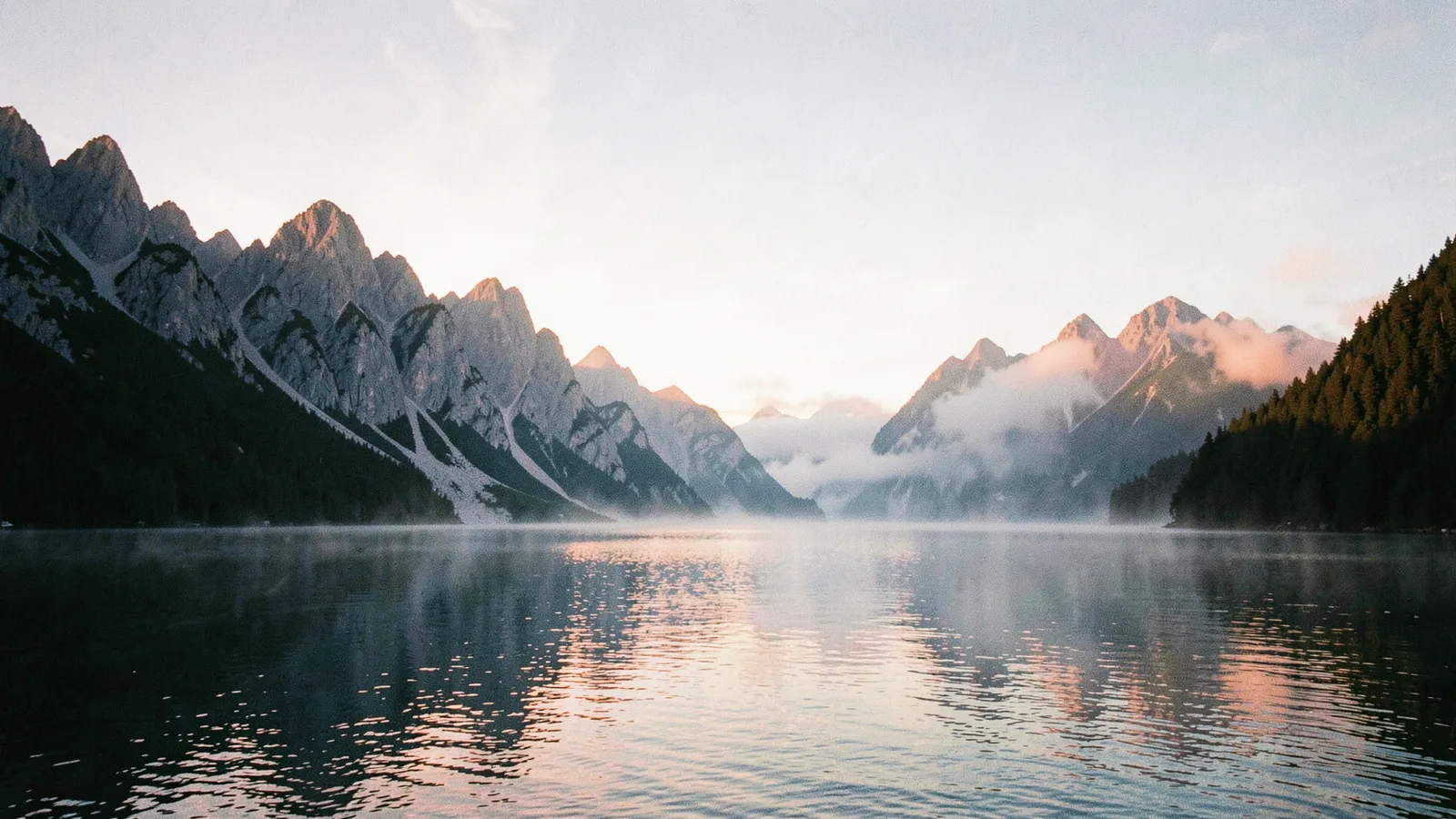 alpine lake at dawn, mist on the water, jagged peaks, pastel sky, 35mm film look